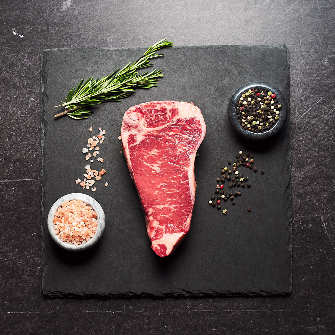 Juicy bone-in New York Strip with salt, pepper, and rosemary on the side