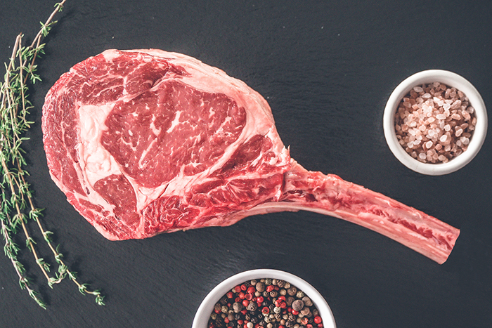 Cowboy Ribeye with rich marbling alongside salt, pepper, and thyme