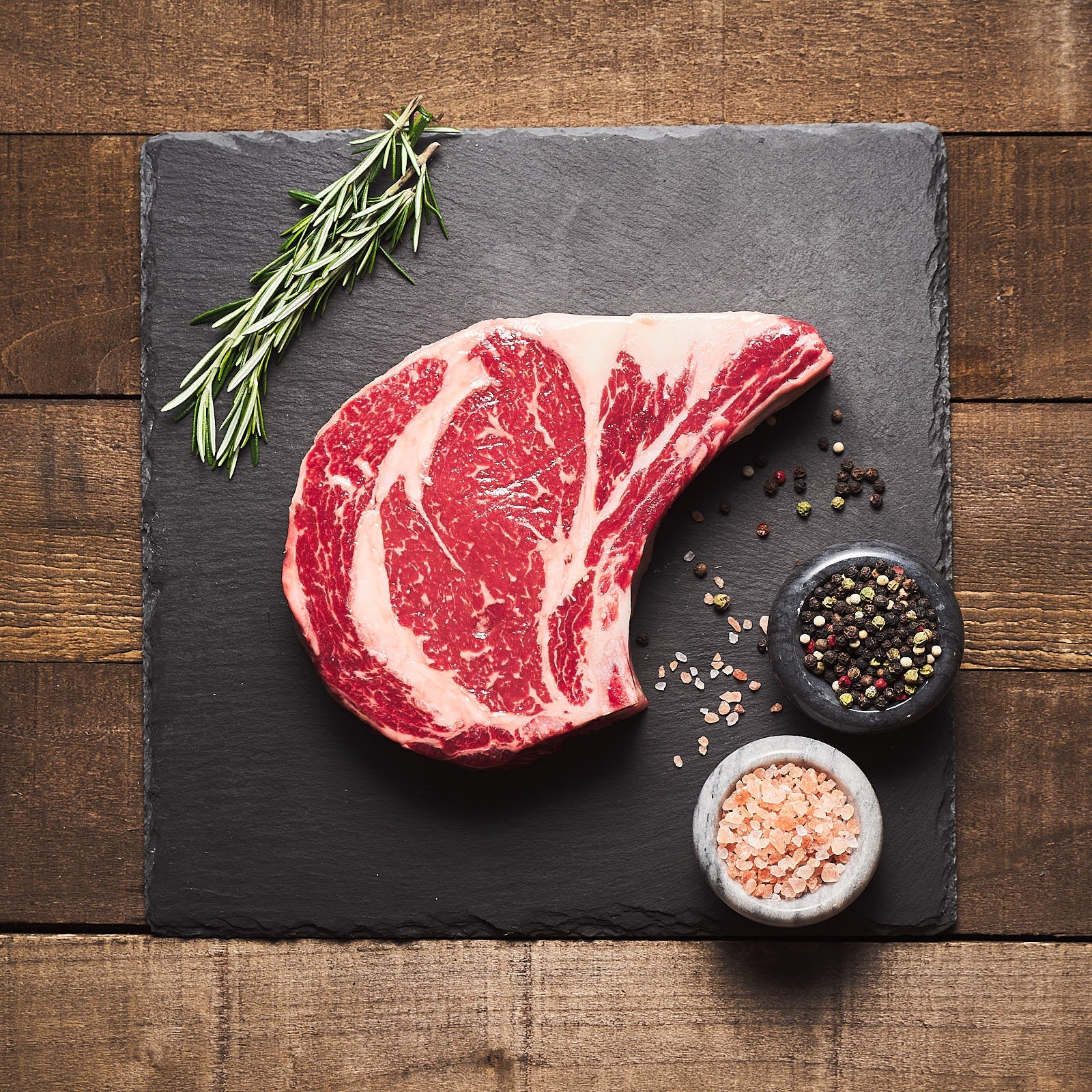 Well-marbled ribeye beside pink Himalayan salt, pepper, and rosemary