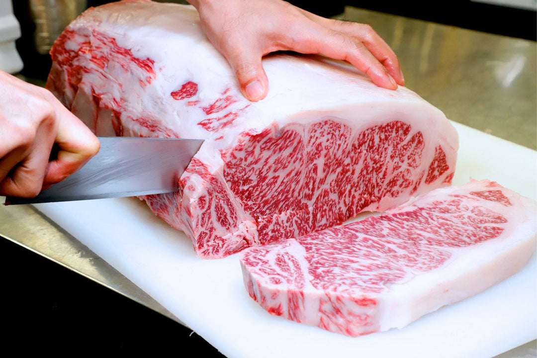 Large cut of intensely marbled wagyu being sliced into strip steaks