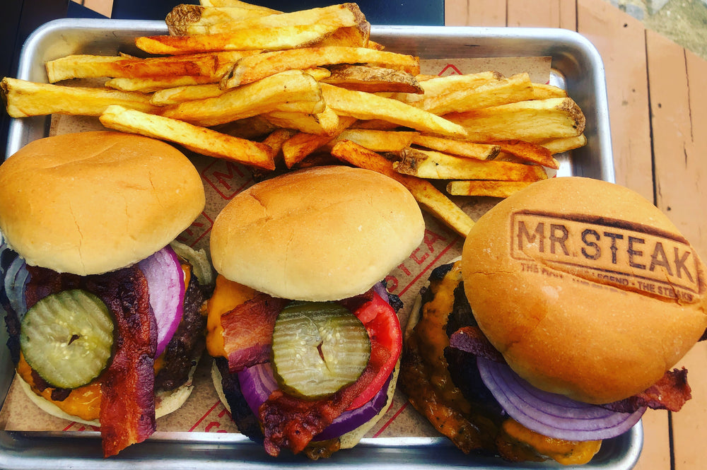 Three juicy cheeseburgers with bacon, pickles, tomatoes, onions with Mr. Steak branding on bun