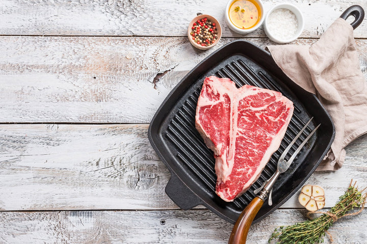 Richly marbled T-bone on a pan with garnishes and aromatics on the side